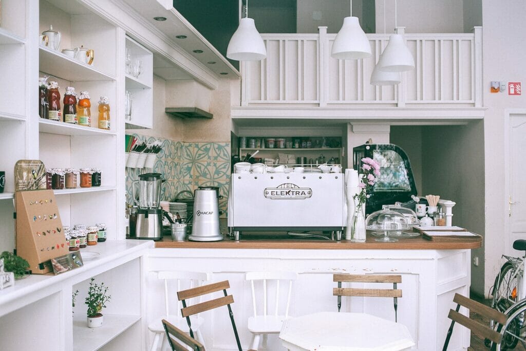 White kitchen set with coffee maker and appliances in small cozy coffee shop with flowers and table in daylight