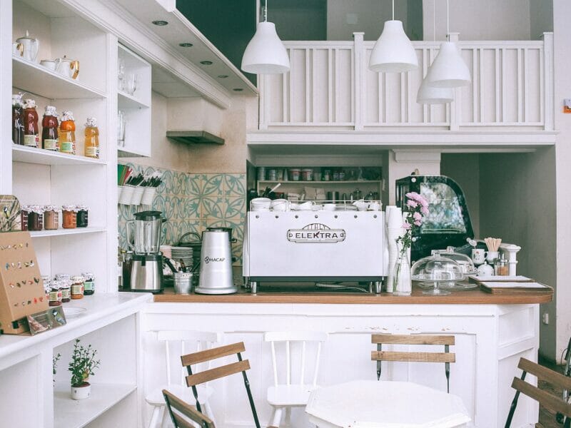 White kitchen set with coffee maker and appliances in small cozy coffee shop with flowers and table in daylight