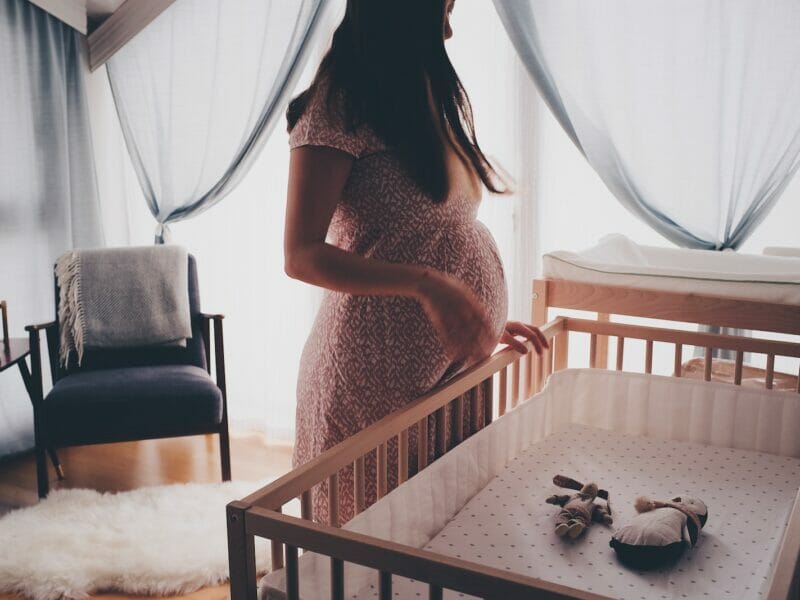 woman in white lace sleeveless dress standing beside brown wooden crib