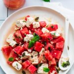 a plate of watermelon and feta salad next to a glass of water