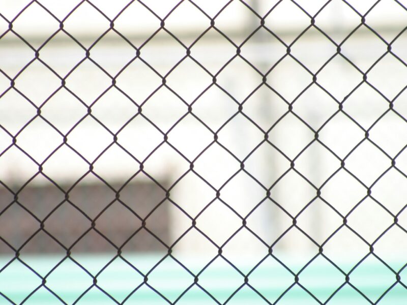 a close up of a chain link fence with a building in the background