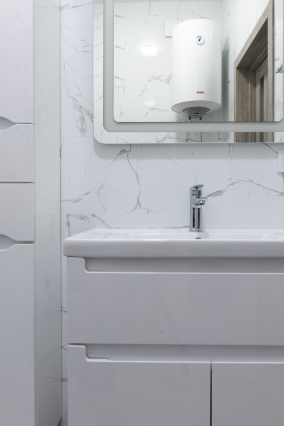 Modern bathroom interior with white washbasin and tap under mirror reflecting water heater at home