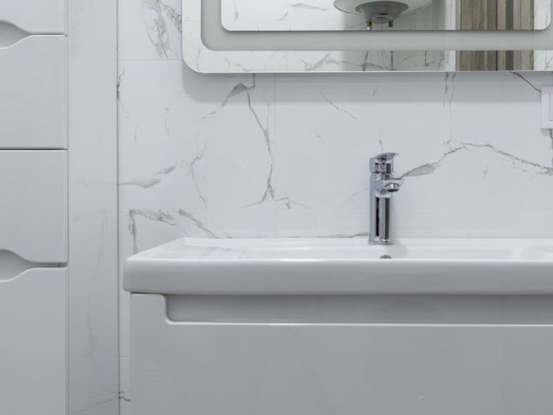Modern bathroom interior with white washbasin and tap under mirror reflecting water heater at home