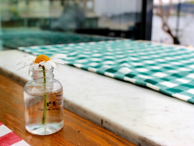 Oxeye daisy in clear glass jar near white and blue textile