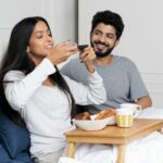 a man and woman sitting on a bed eating food