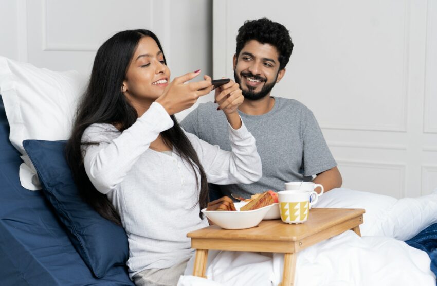 a man and woman sitting on a bed eating food