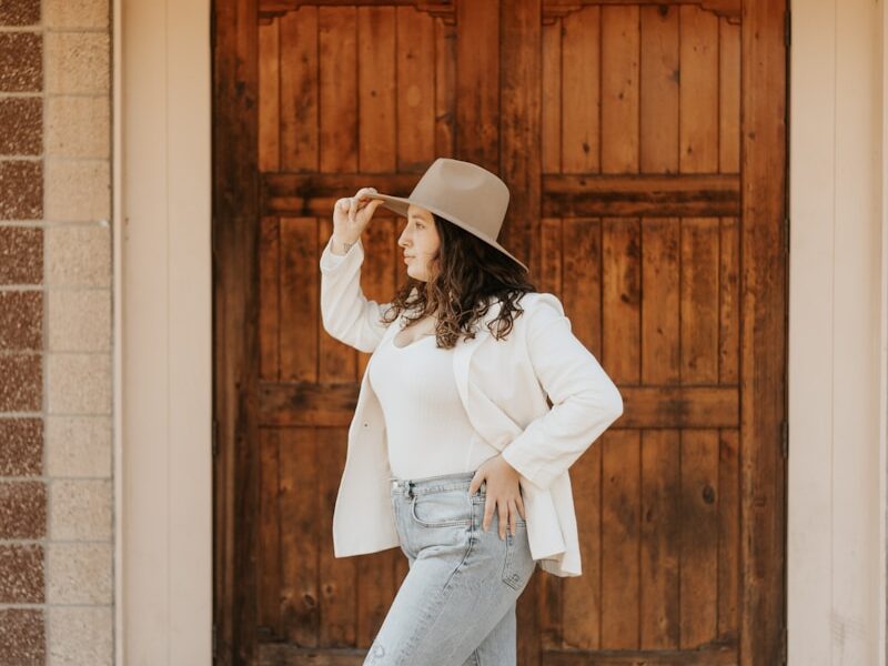woman in white long sleeve shirt and blue denim jeans standing near brown wooden door