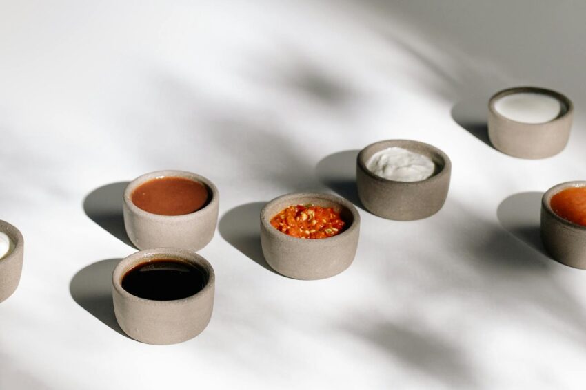 A variety of sauces in ceramic bowls under natural sunlight casting artistic shadows.