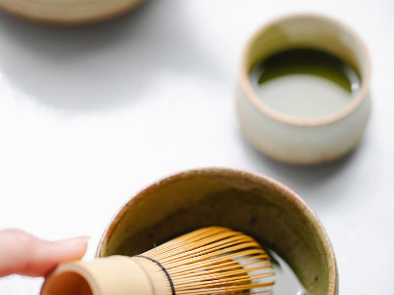 Close-up of hands preparing matcha tea with whisk and cup, indoors.