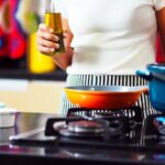 person holding bottle of oil at gas stove