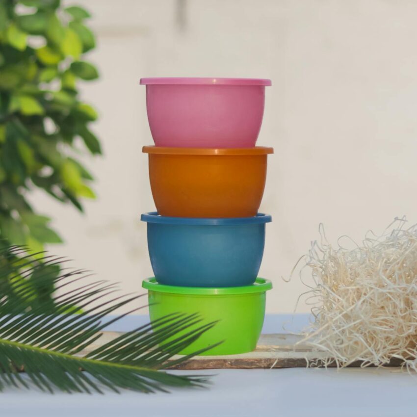 A vibrant stack of colorful plastic containers outdoors, surrounded by plants and straw.