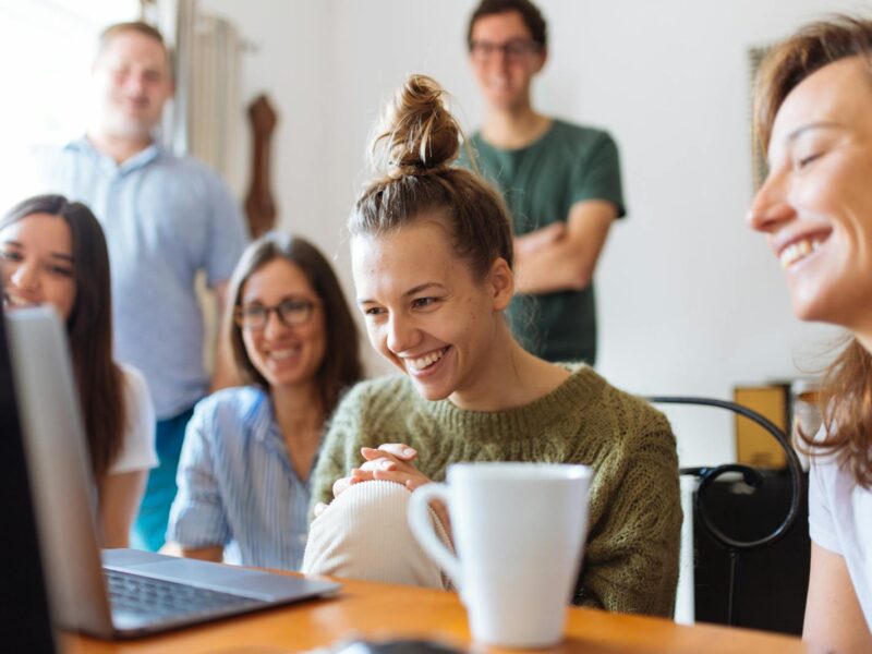 A group of friends enjoying a moment together indoors, smiling and watching a video on a laptop.