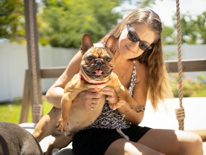 woman in black and white leopard print tank top carrying brown pug