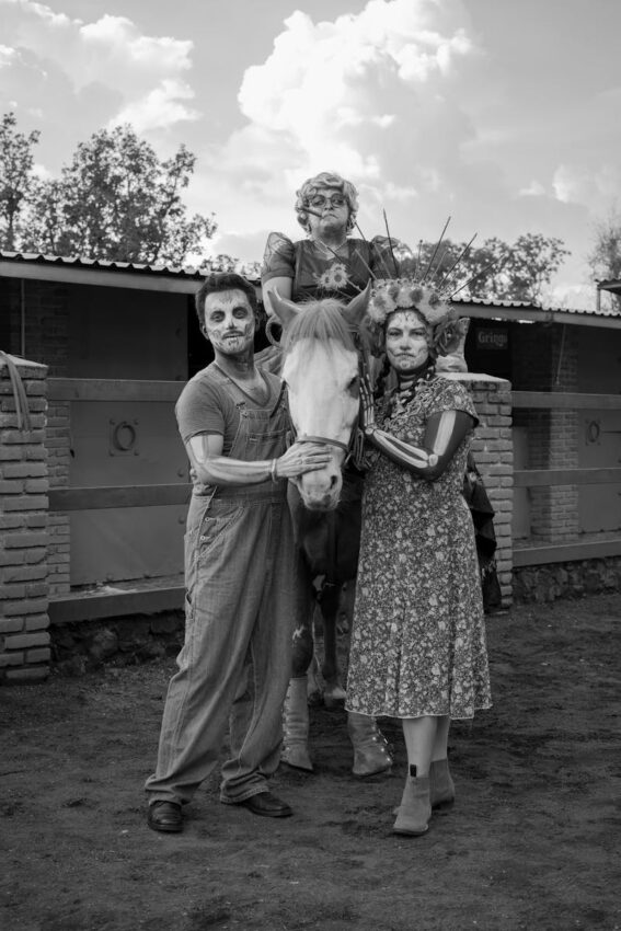 A grayscale image of a zombie-themed family posing with a horse outdoors.