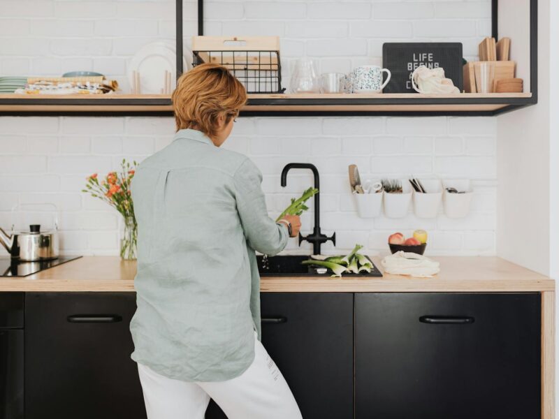 A woman standing at a kitchen counter preparing fresh vegetables. Modern and vibrant home interior.