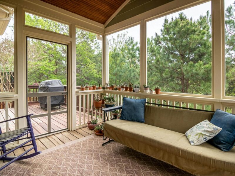 Relaxing screened porch with couch, plants, and outdoor greenery view.