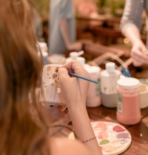 Adults painting pottery in a creative workshop setting, focusing on detail and artistry.