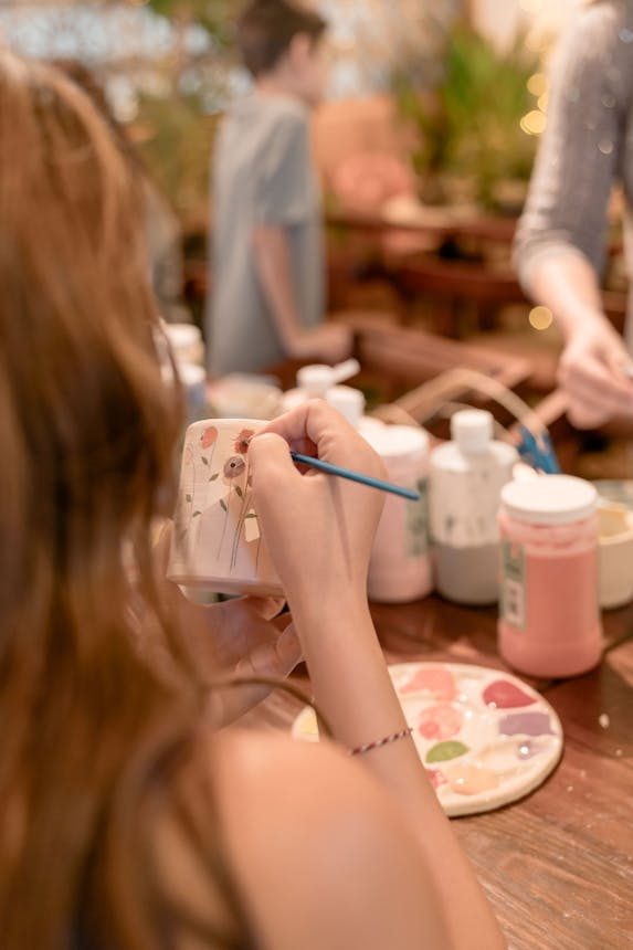 Adults painting pottery in a creative workshop setting, focusing on detail and artistry.