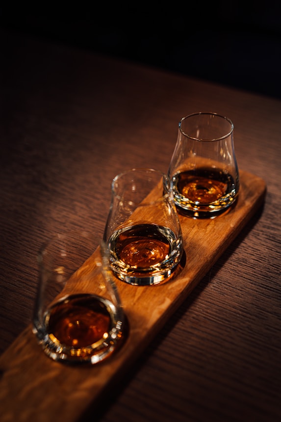 Three glasses of whiskey sitting on a wooden tray