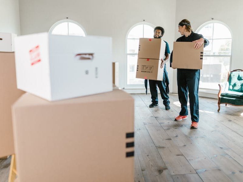 Two movers in uniform carrying boxes in a bright, new home setting.