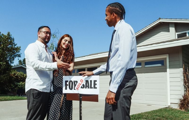 A couple meets with a realtor to finalize the purchase of their new home, indicated by a 'Sold' sign.