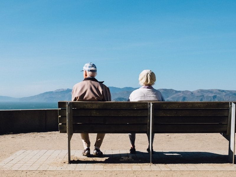 man and woman sitting on bench facing sea