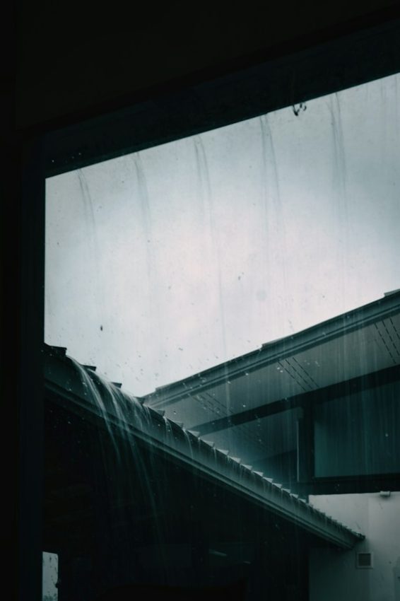 Heavy rain streams down a roof and window pane