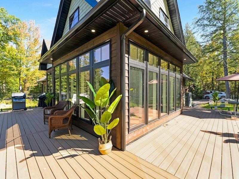 A wooden deck with wicker chairs and a potted plant beside a house