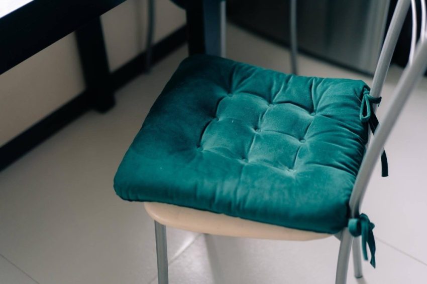 A teal tufted seat cushion tied to a chair beside a table.